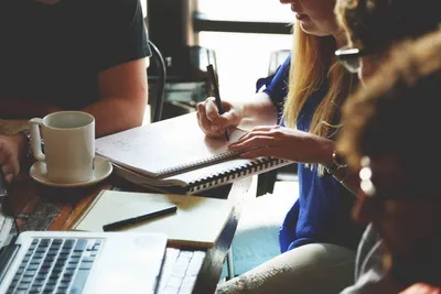 People collaborating with notebooks, laptop, and coffee in a casual work setting.